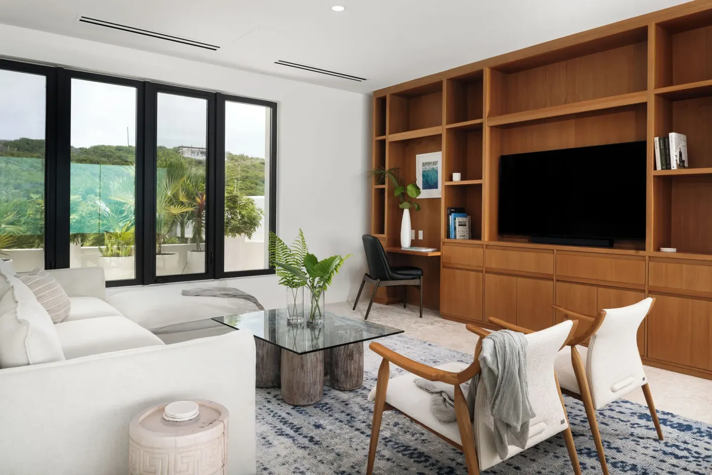 Garden-view lounge with white sofa and wood media shelving at The Strand Turks and Caicos.