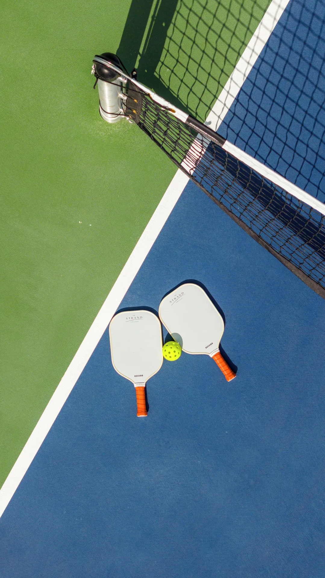 Pickleball paddles and a ball on a blue and green court at The Strand Turks and Caicos.