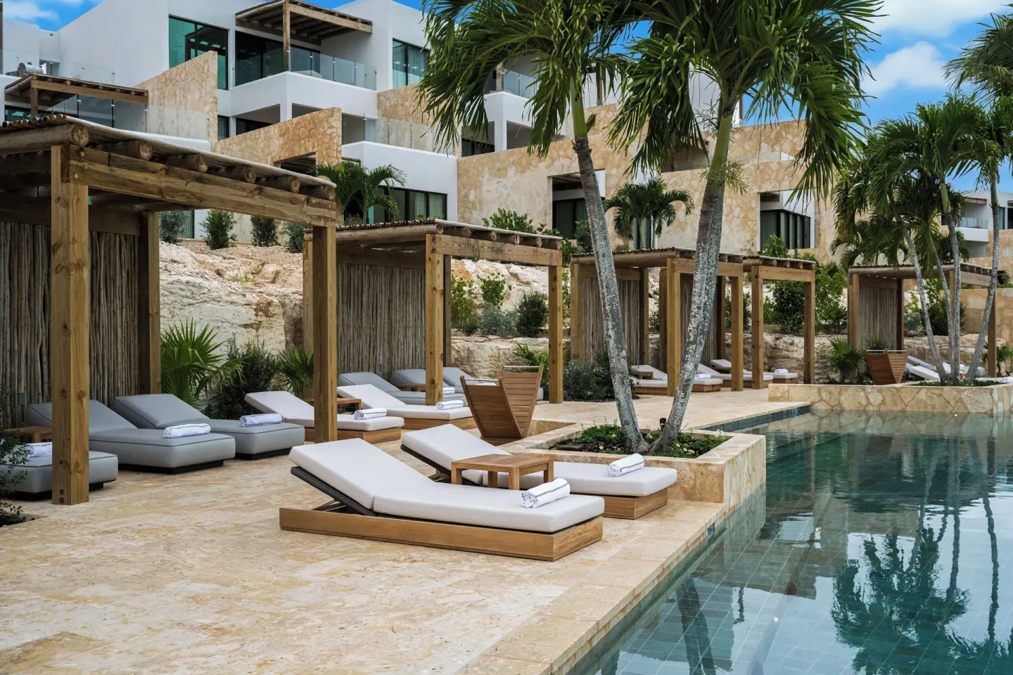 Poolside loungers and cabanas below resort buildings at The Strand Turks and Caicos.