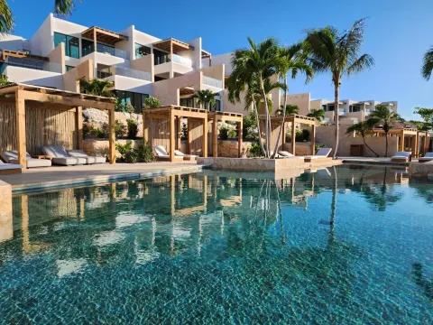 Resort pool with cabanas, palms, and hillside buildings at The Strand Turks and Caicos.