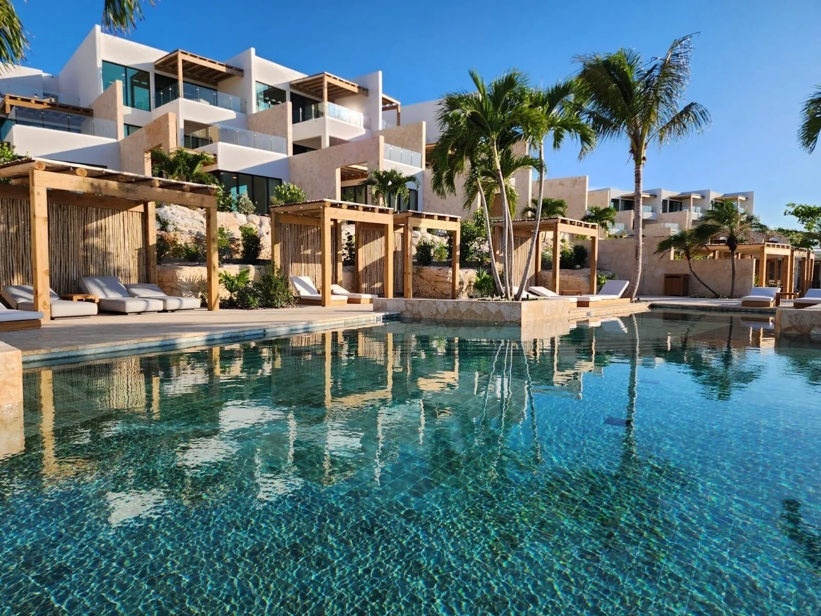 Resort pool with cabanas, palms, and hillside buildings at The Strand Turks and Caicos.