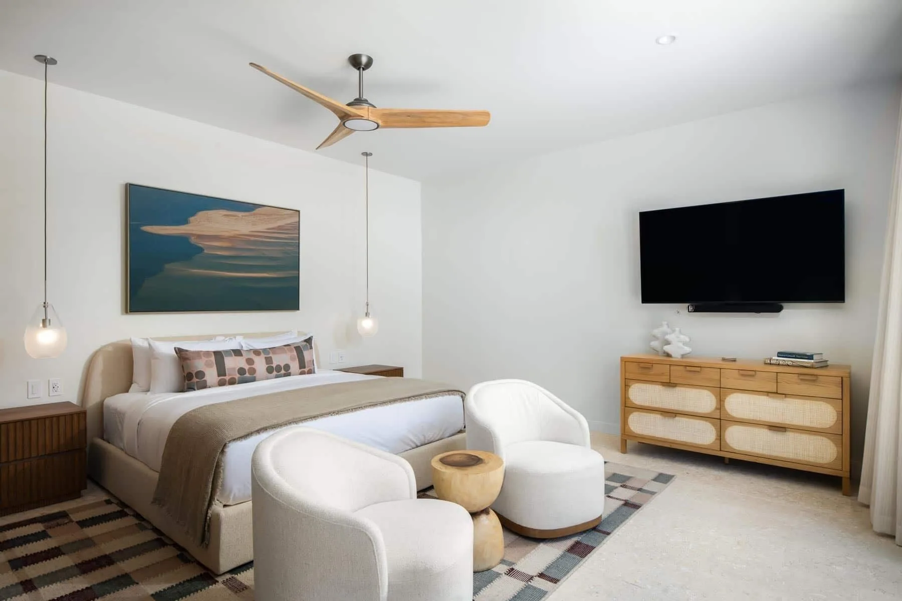 King bedroom with lounge chairs and wall-mounted TV at The Strand Turks and Caicos.