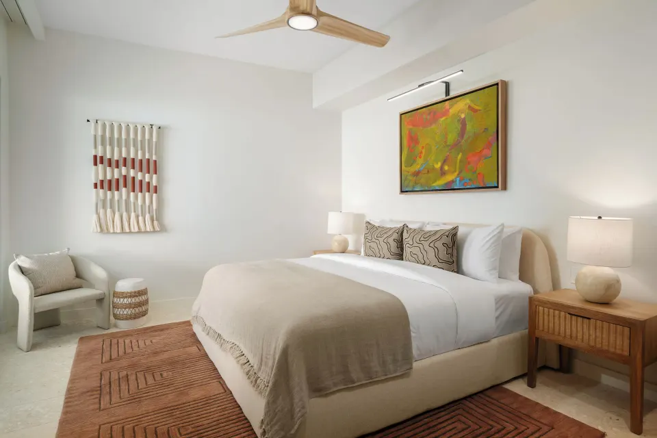 One-bedroom suite king bed with lounge chair and ceiling fan at The Strand Turks and Caicos.