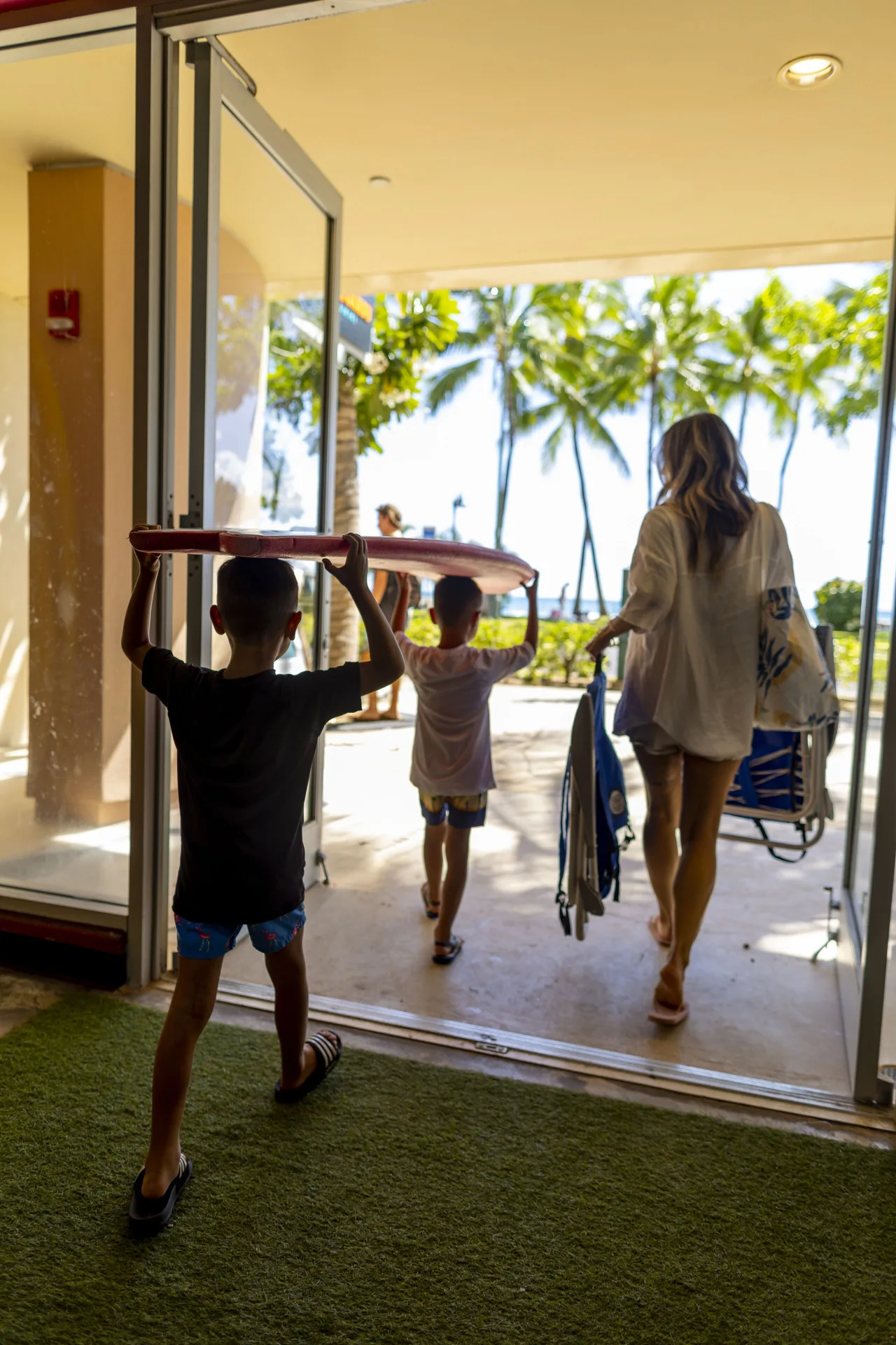 Family carrying beach gear toward palm trees at The Twin Fin Hotel.