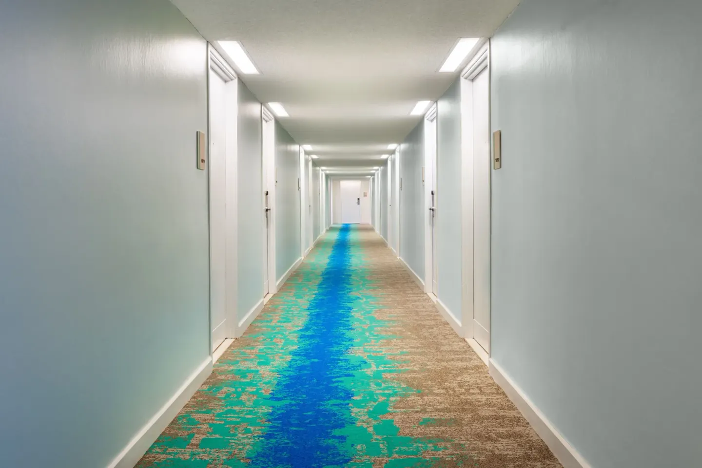 Guest corridor with blue-and-turquoise carpet at The Twin Fin Hotel.