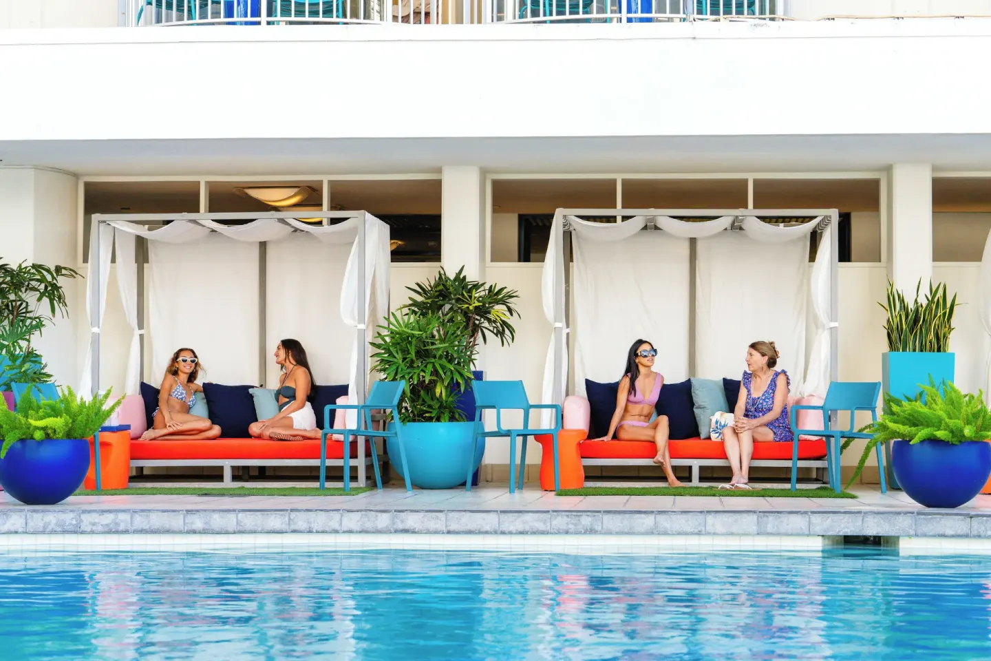 Poolside cabanas with guests and colorful planters at The Twin Fin Hotel.