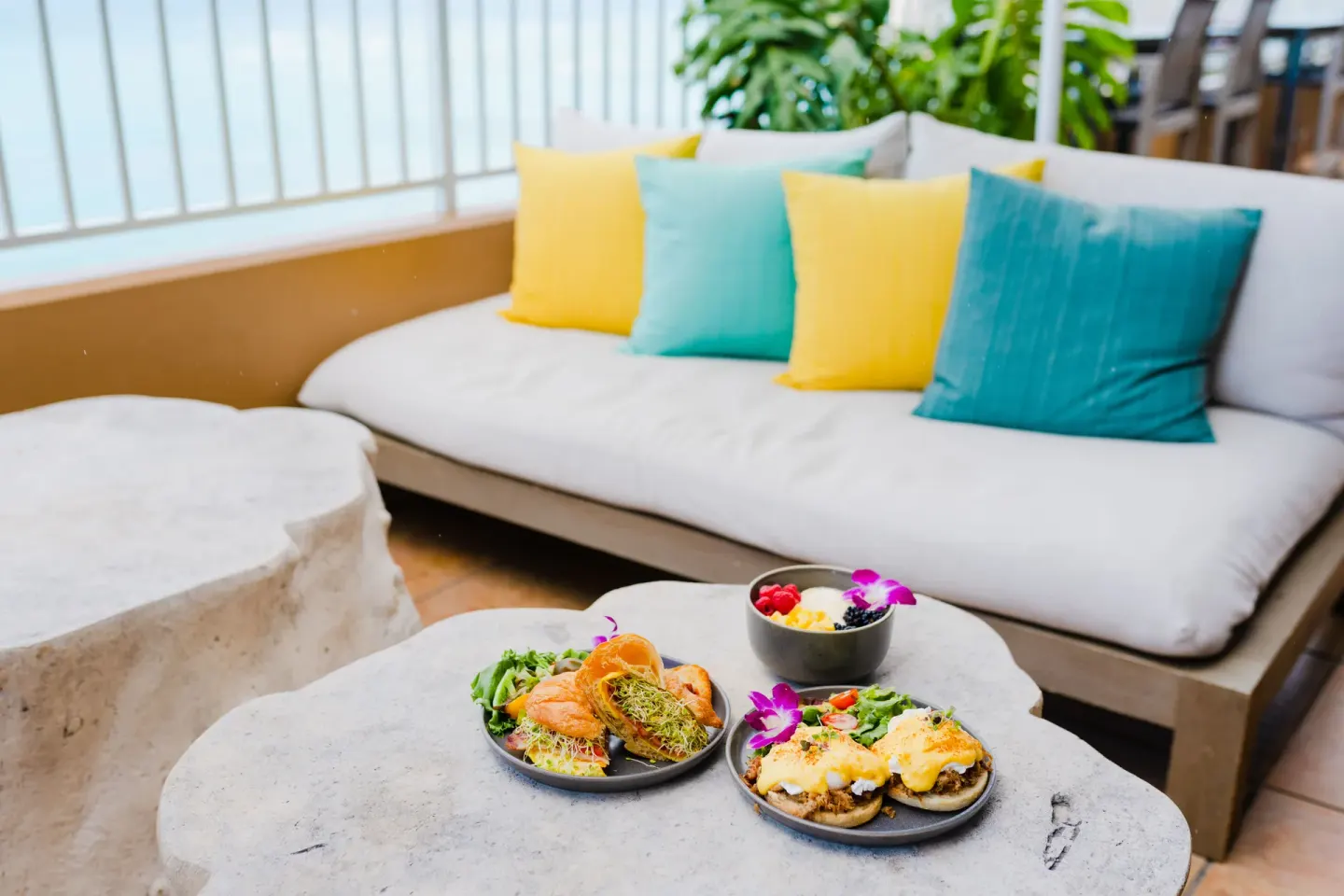 Breakfast plates on a stone table by colorful lounge pillows at The Twin Fin Hotel.