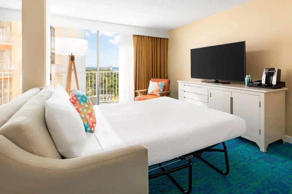 Junior Suite sofa bed, TV console, balcony, and partial ocean view at The Twin Fin Hotel.