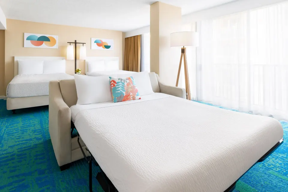 Junior Suite with sofa bed, two beds, floor lamp, and bright windows at The Twin Fin Hotel.