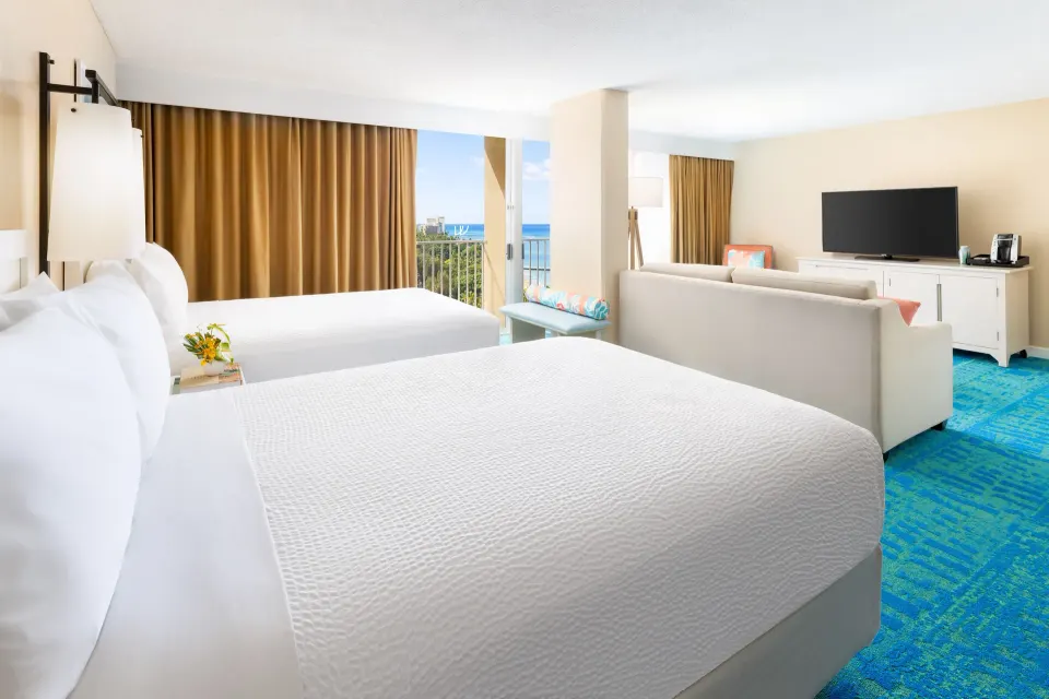 Junior Suite with two beds, sofa, balcony, and partial ocean view at The Twin Fin Hotel.