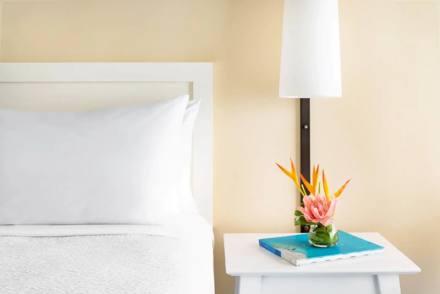 Bedside table with flowers beside a white bed in a City View room at The Twin Fin Hotel.
