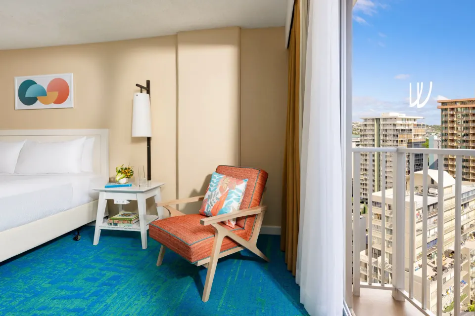 Bed, orange lounge chair, and balcony city view in a City View room at The Twin Fin Hotel.