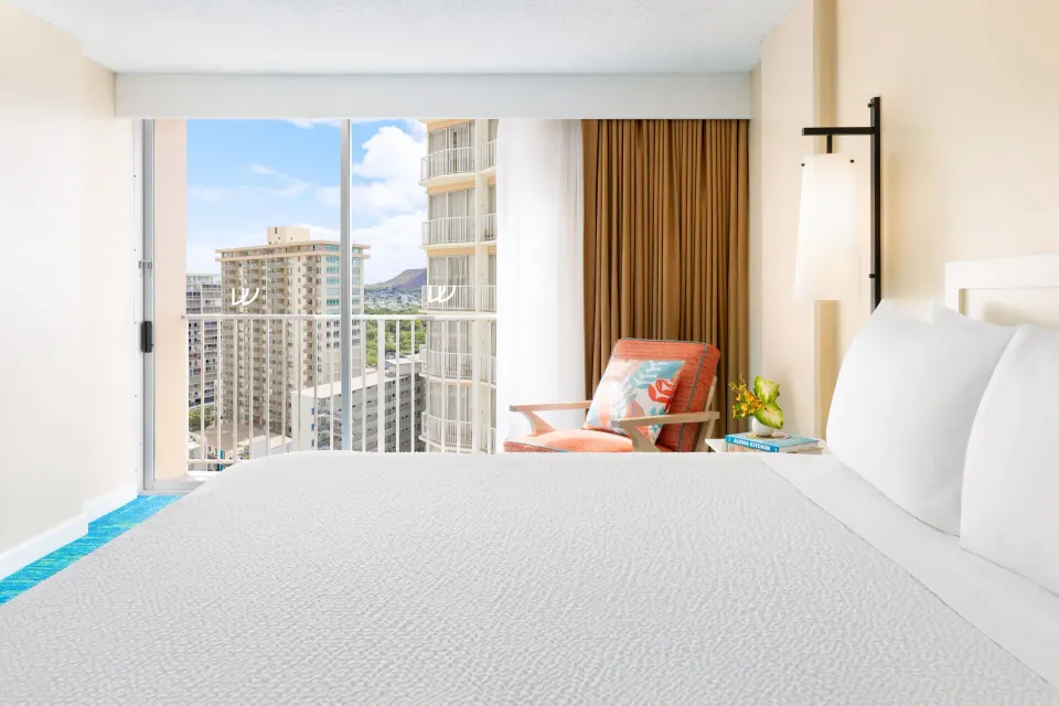 White bed, lounge chair, and city view window in a City View room at The Twin Fin Hotel.