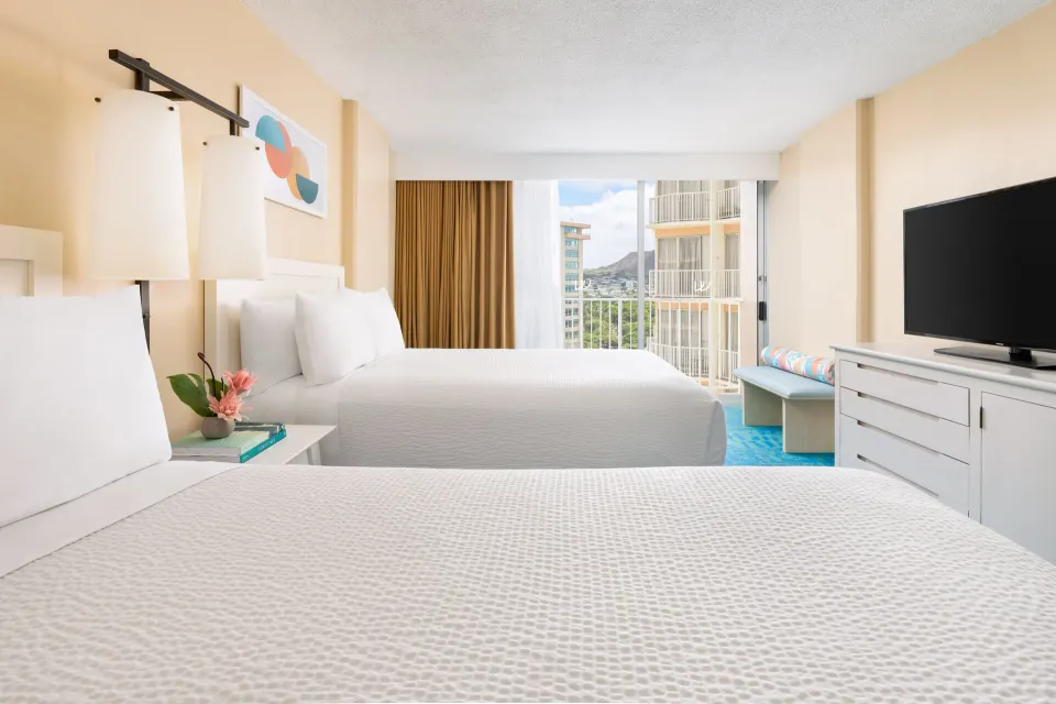 Two beds, TV dresser, and city-facing window in a City View room at The Twin Fin Hotel.
