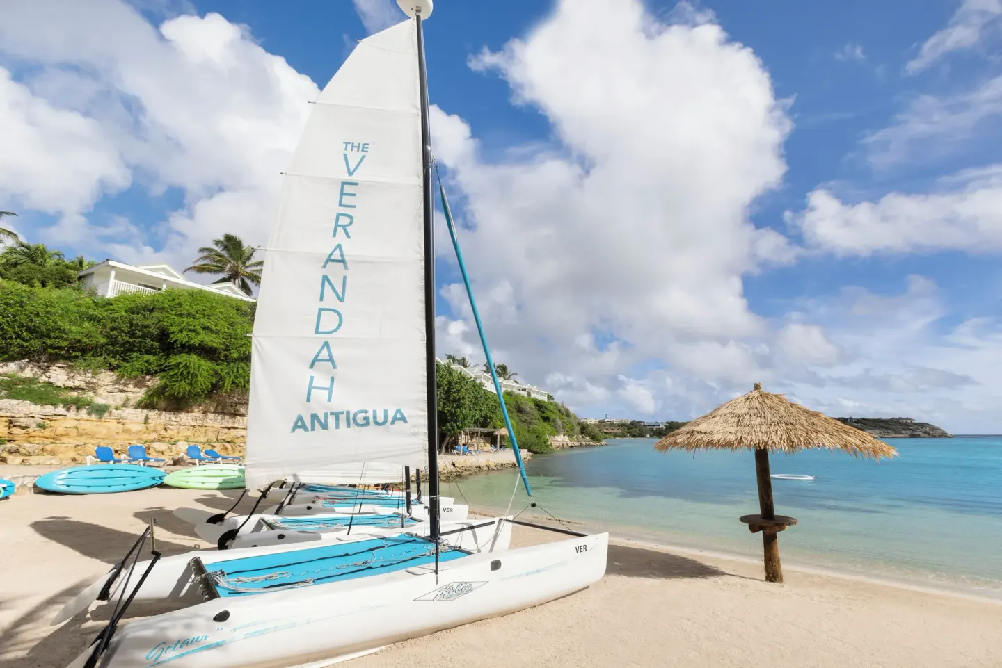White catamaran sailboat on the beach beside a thatched umbrella at The Verandah Antigua.