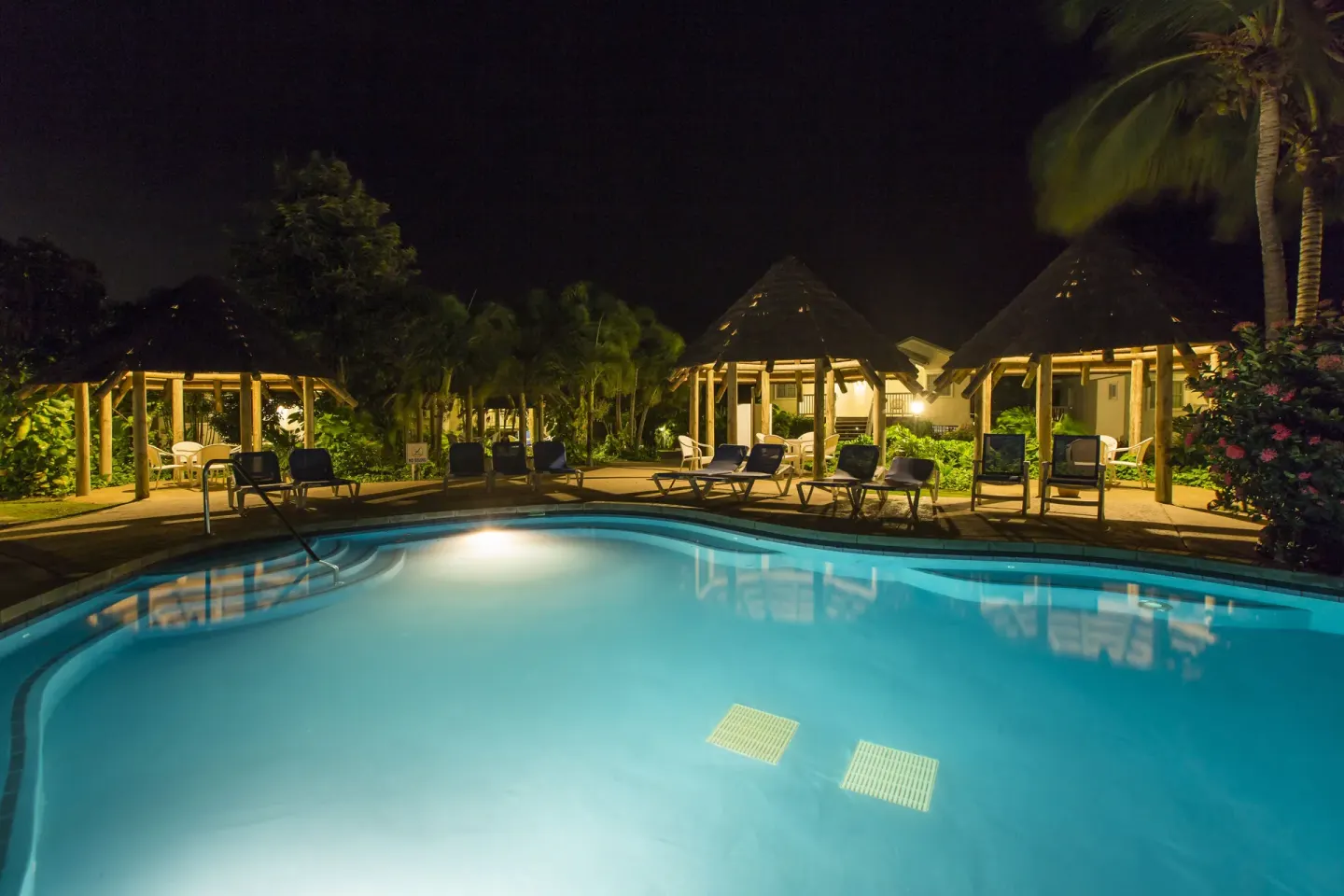 Illuminated pool with lounge chairs and gazebos at night at The Verandah Antigua.
