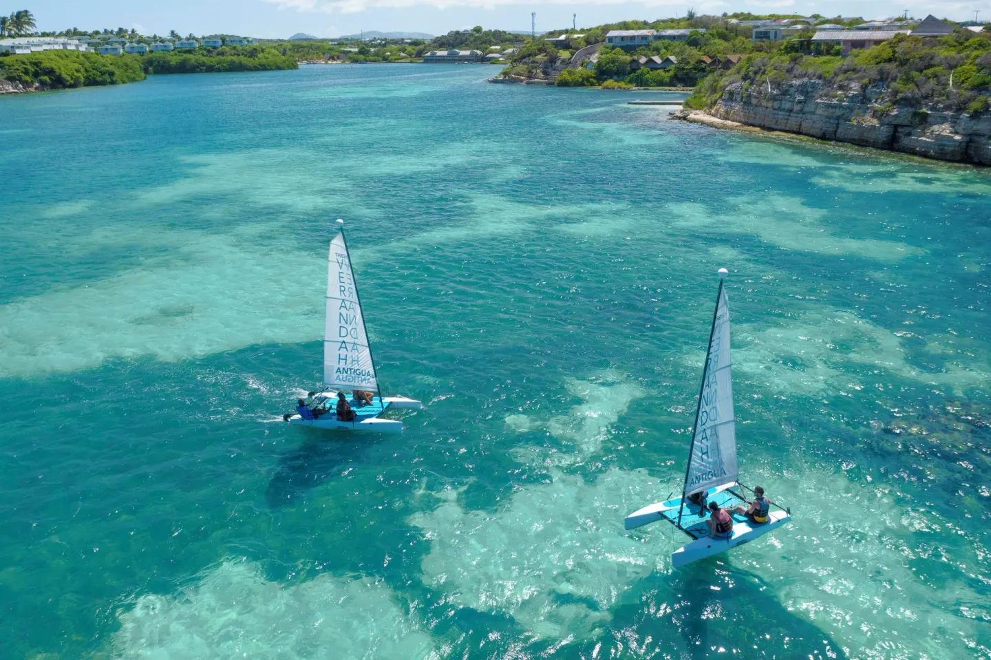 Two small sailboats moving across turquoise water near The Verandah Antigua.