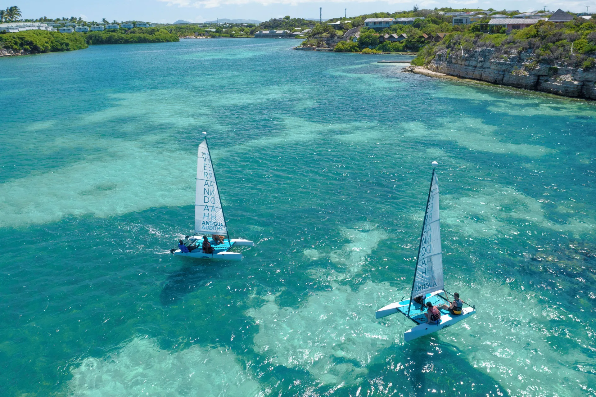 Two small sailboats moving across turquoise water near The Verandah Antigua.