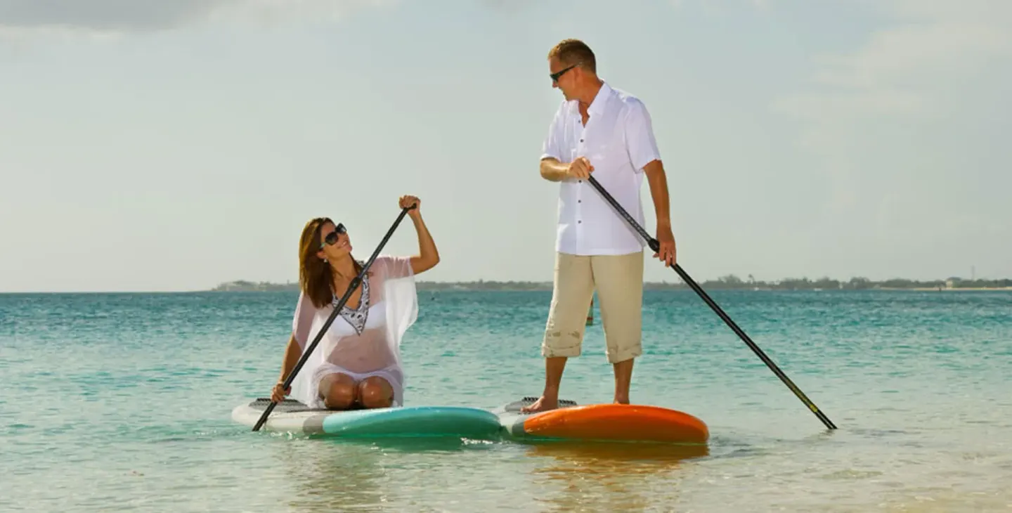 Guests paddleboarding in turquoise water at The Westin Grand Cayman Seven Mile Beach Resort & Spa.