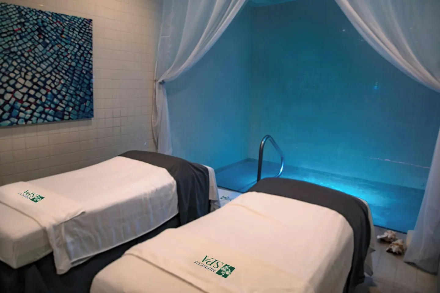 Twin spa beds beside a blue-lit pool at The Westin Grand Cayman Seven Mile Beach Resort & Spa.