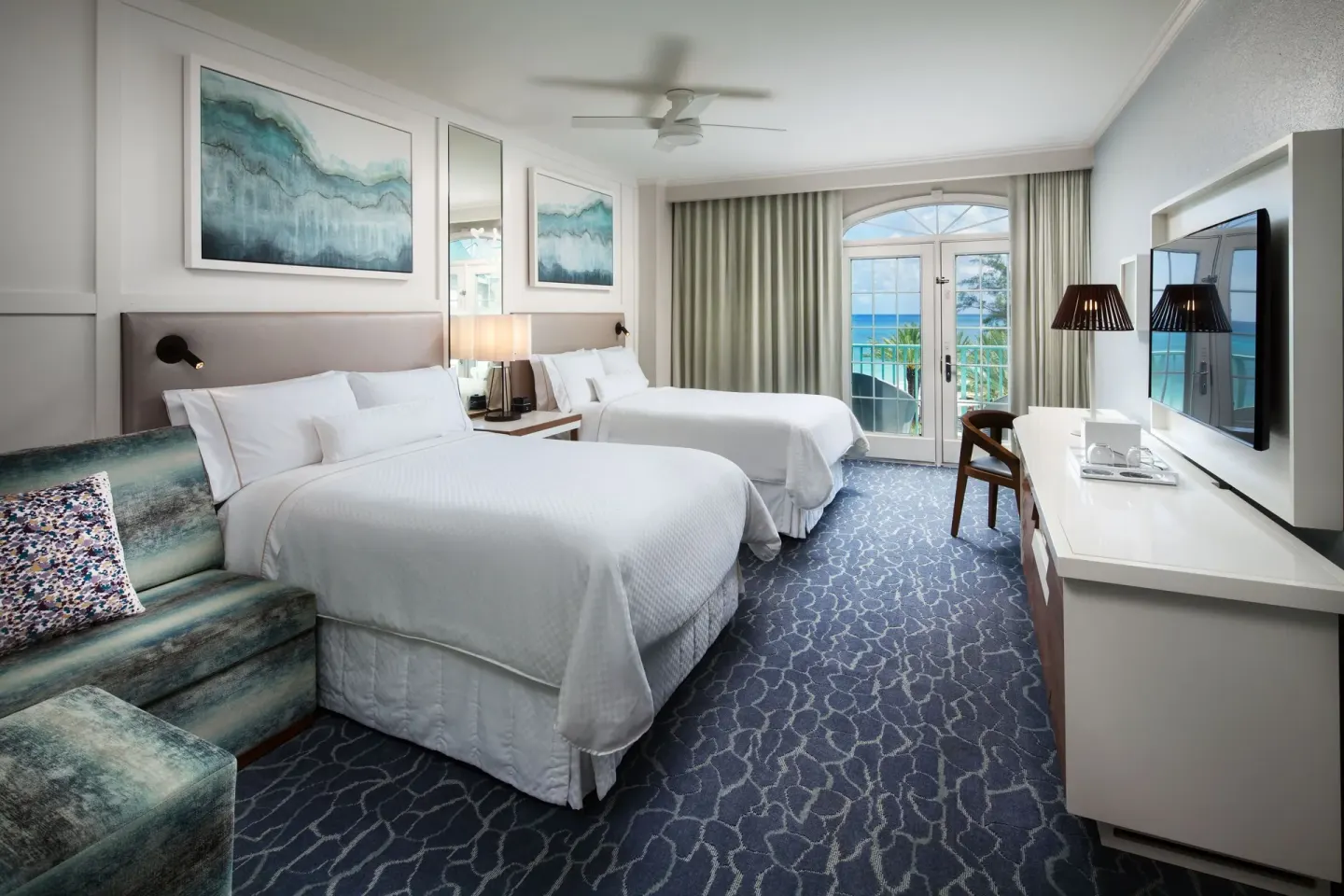 Two queen beds, sofa, and balcony view in a room at The Westin Grand Cayman Seven Mile Beach Resort & Spa.