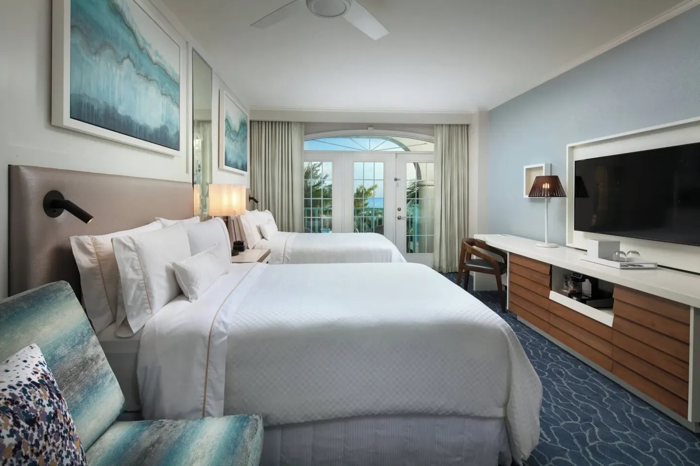 Two-bed guest room with ocean glimpses through balcony doors at The Westin Grand Cayman Seven Mile Beach Resort & Spa.