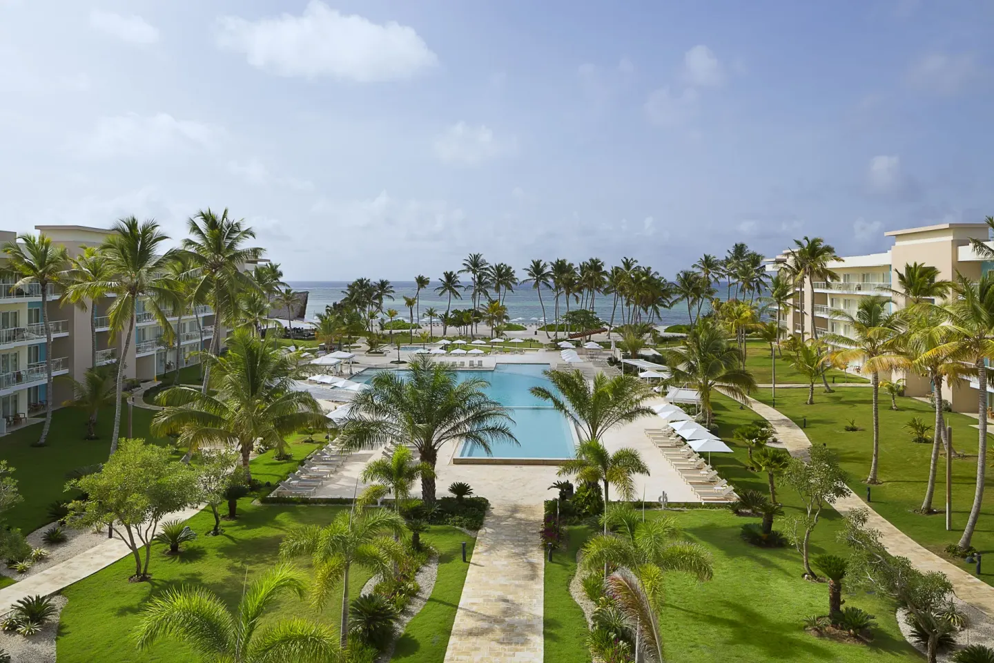 Daytime pool courtyard with palms and ocean beyond at The Westin Puntacana Resort.