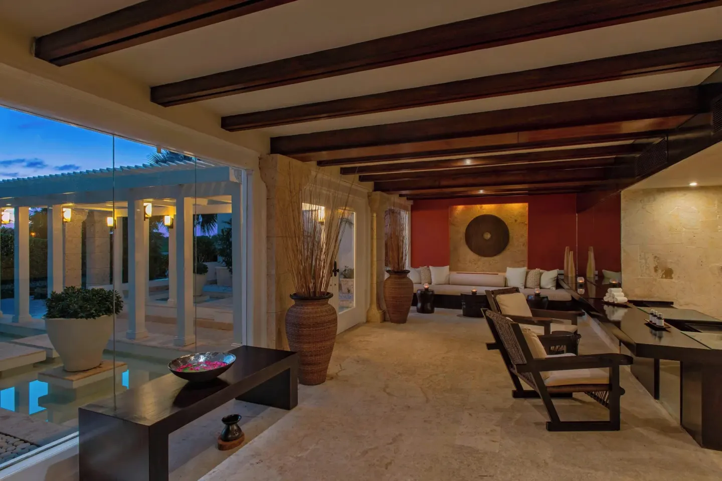Warm indoor lounge at The Westin Puntacana Resort with wood beams, sofas and glass walls at dusk.