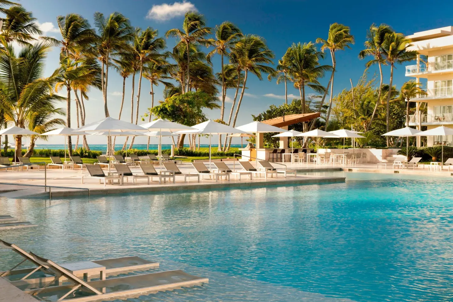 Pool deck with umbrellas, palms, and ocean beyond at The Westin Puntacana Resort.