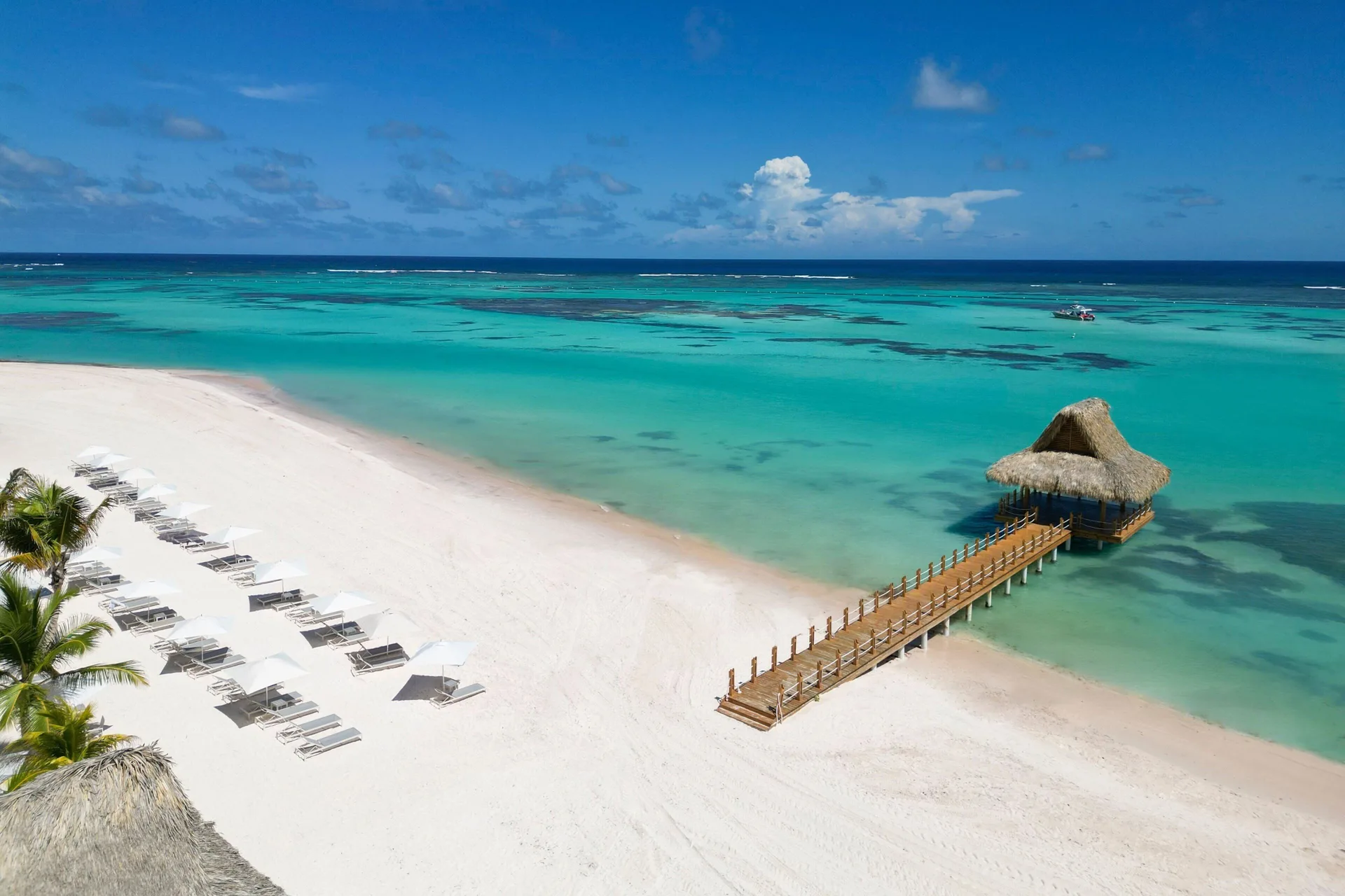 White-sand beach with loungers, turquoise water and a pier at The Westin Puntacana Resort.