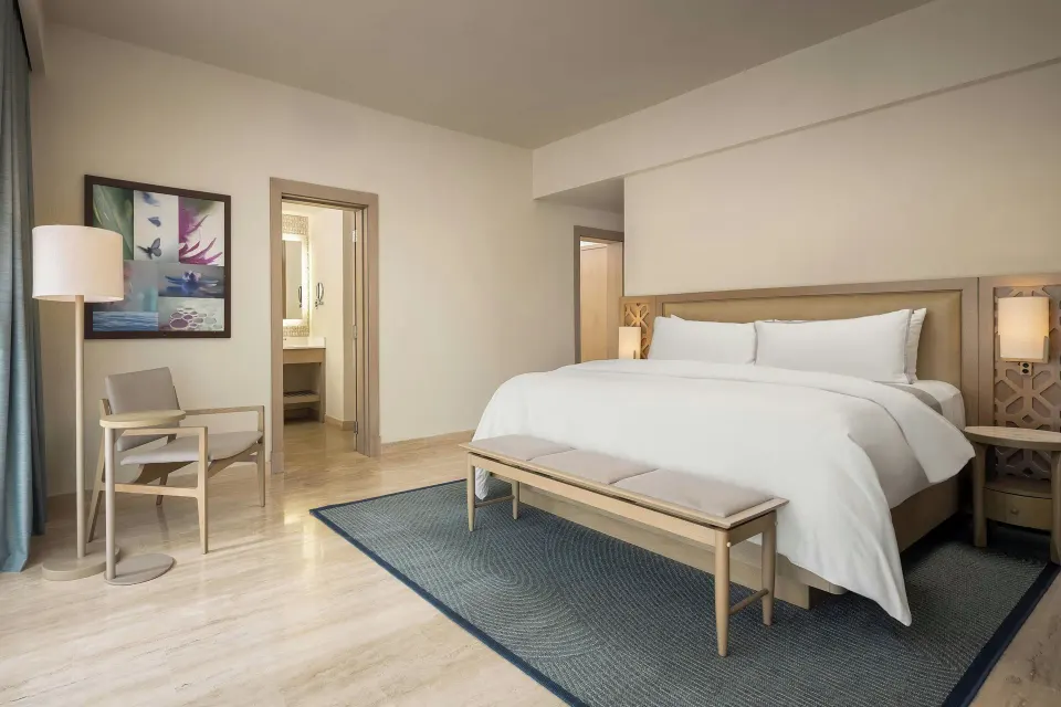 Premium Room king bed with bench, chair, artwork, and bathroom doorway at The Westin Puntacana Resort.
