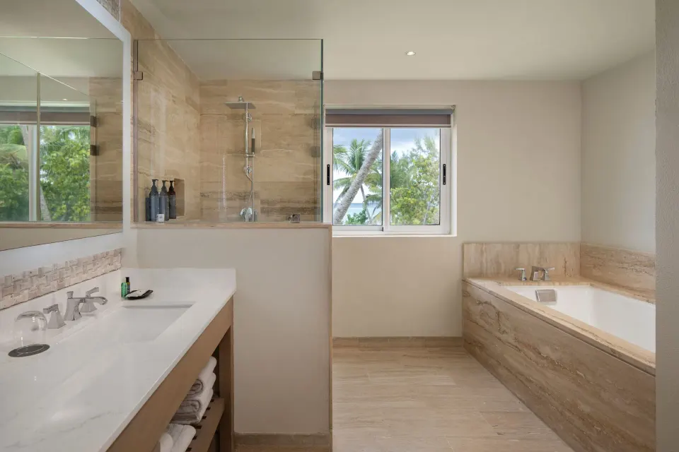 Suite bathroom at The Westin Puntacana Resort with soaking tub, glass shower, vanity, and palm-view window.