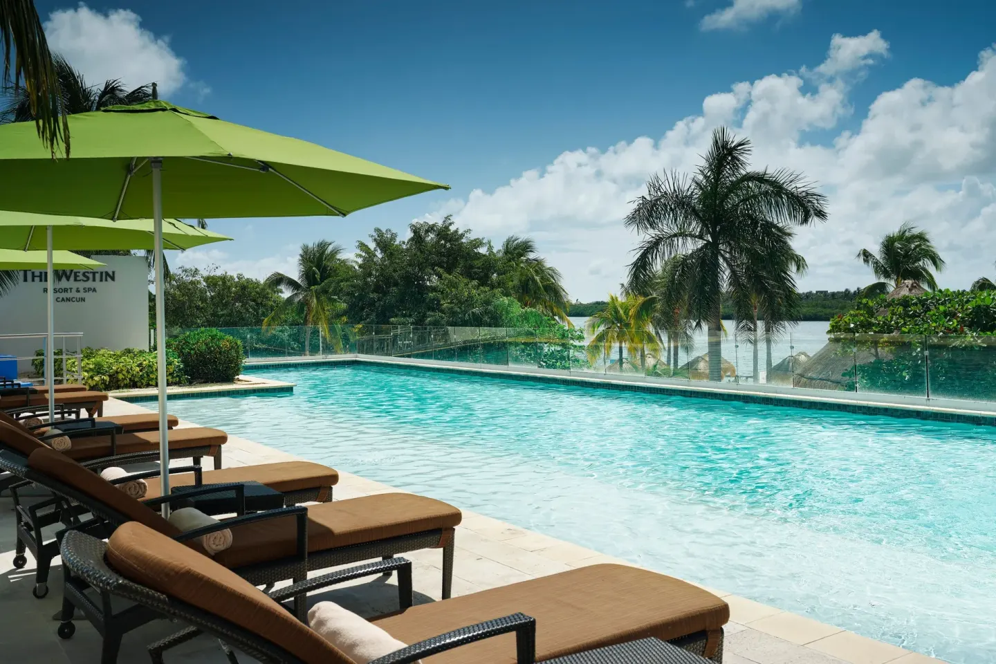 Pool terrace with lounge chairs, green umbrellas, and palms at The Westin Resort & Spa, Cancun.