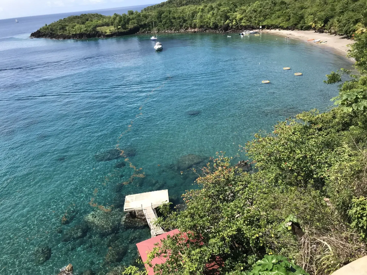 Clear cove water, beach and boats below the hillside at Ti Kaye Resort & Spa.