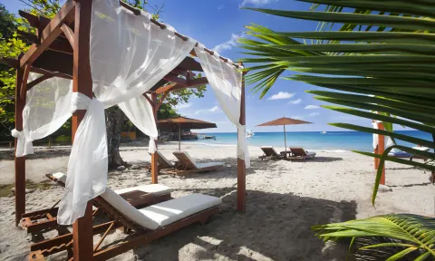White-curtained beach cabana and loungers on the sand at Ti Kaye Resort & Spa.