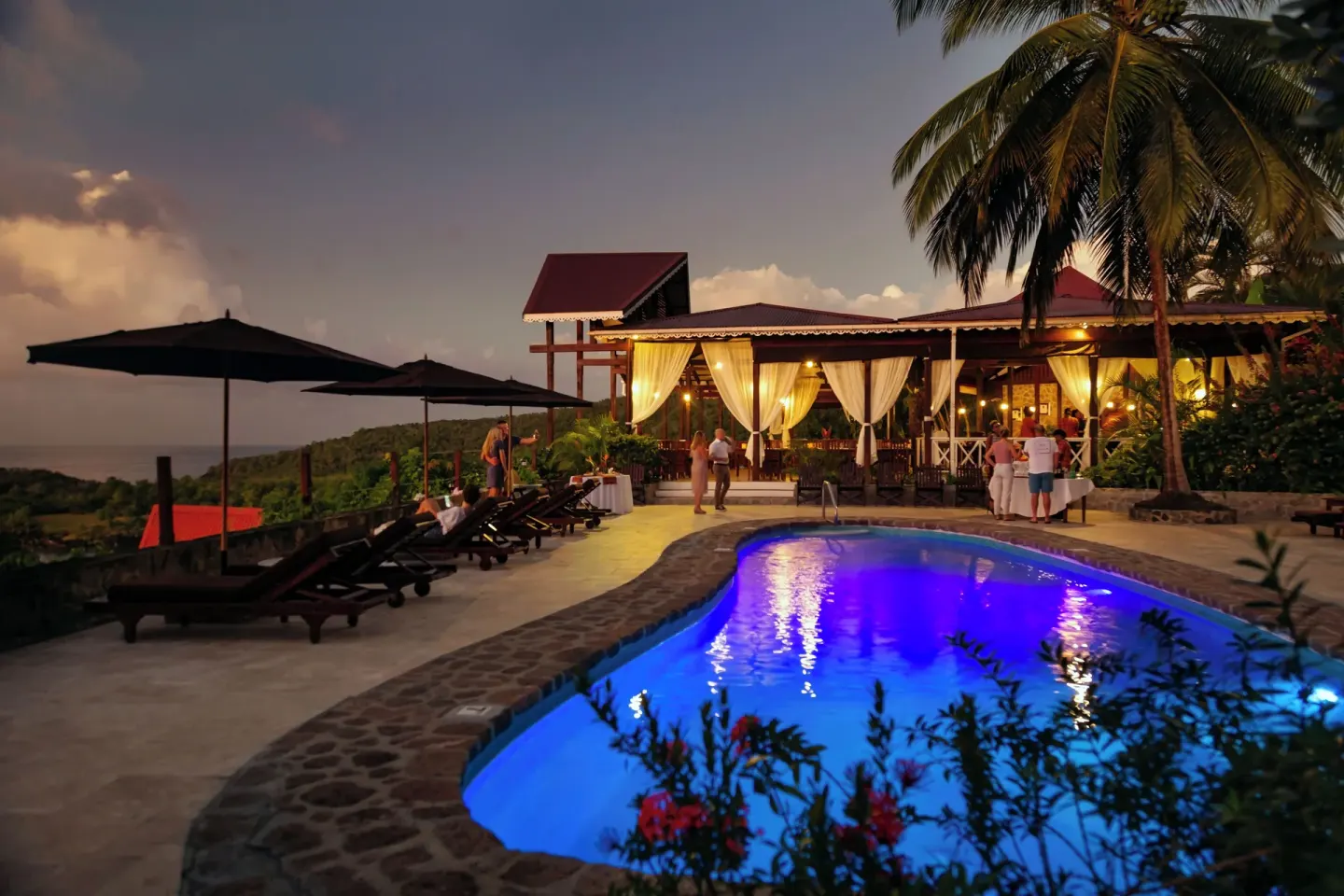 Evening pool scene with loungers and a lit pavilion at Ti Kaye Resort & Spa.