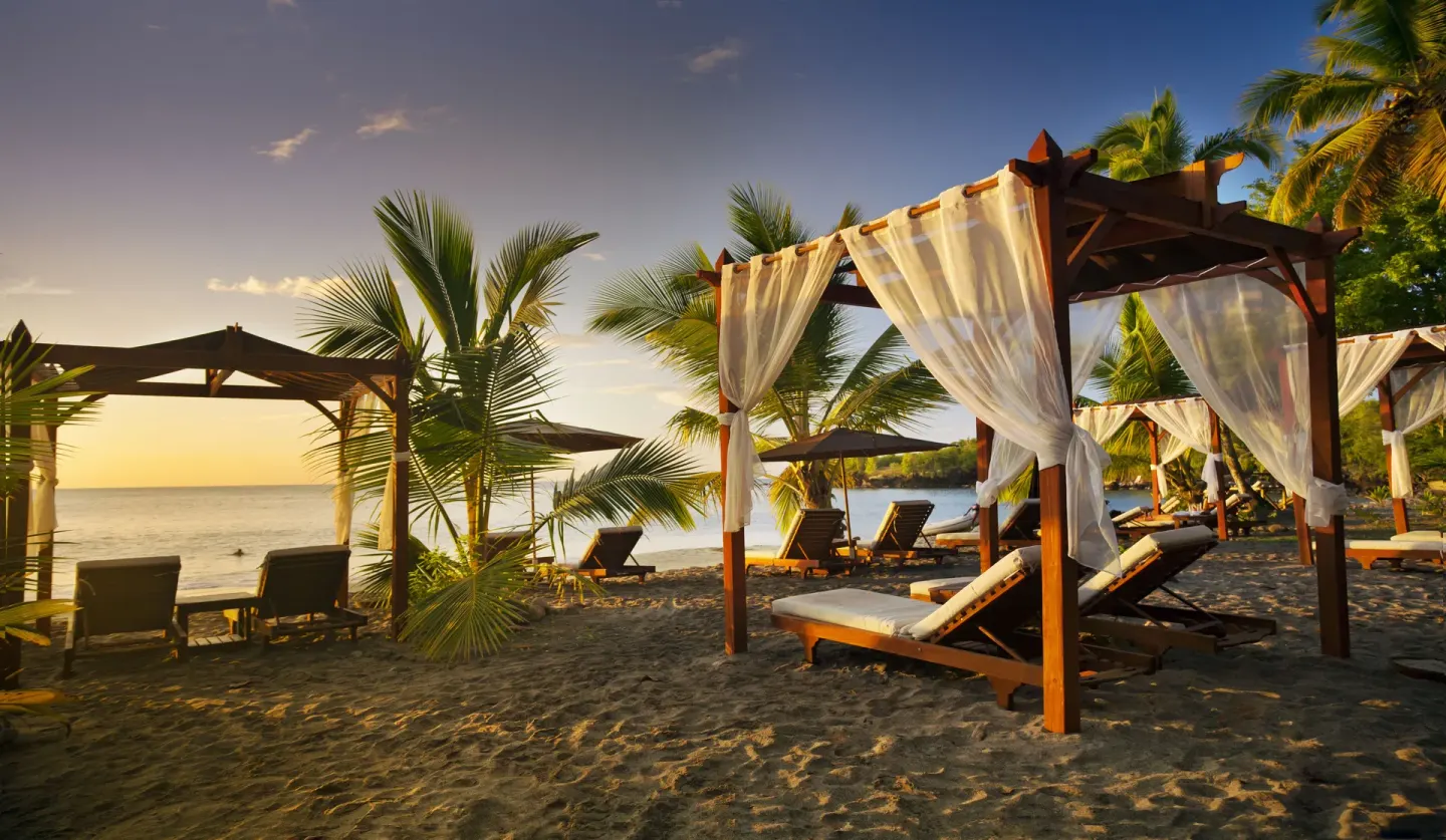 Beach cabanas with loungers and palms at sunset at Ti Kaye Resort & Spa.
