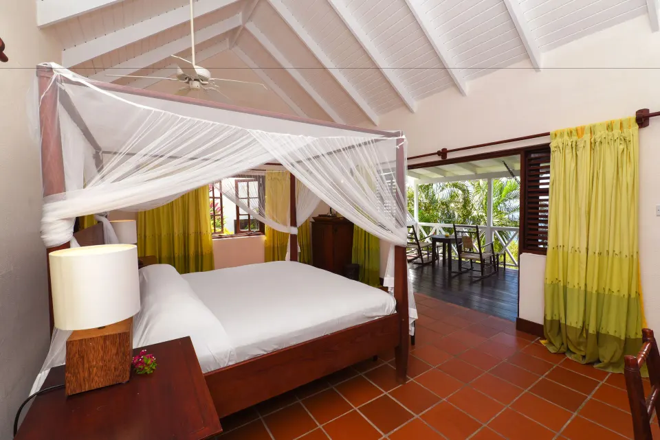 Ocean View Room four-poster bed beside an open balcony at Ti Kaye Resort & Spa.