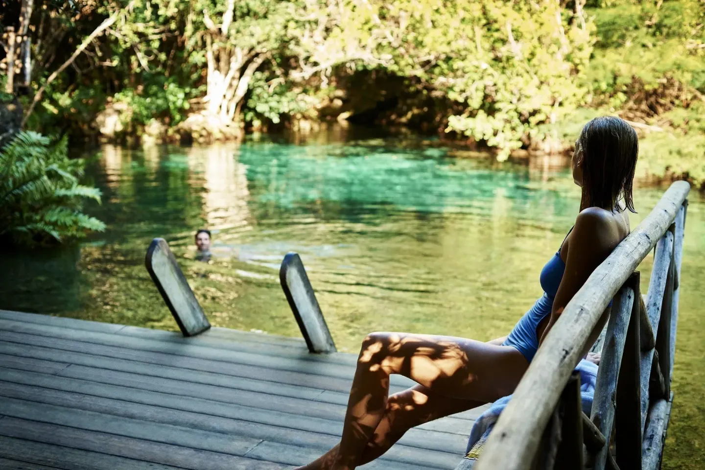 Guest sitting on a wooden deck beside a clear lagoon at Tortuga Bay Hotel.