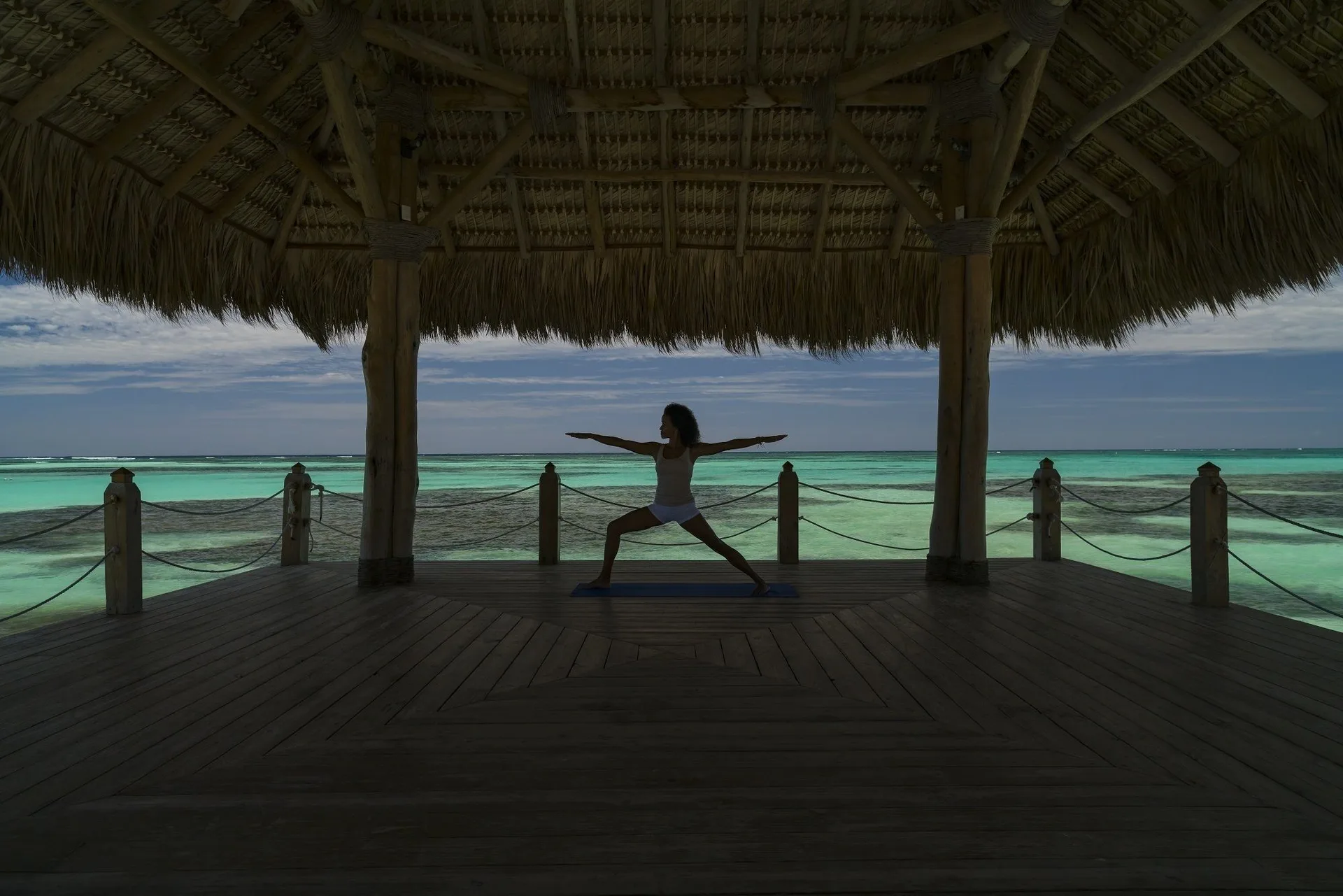 Person practicing yoga in a thatched pavilion over turquoise water at Tortuga Bay Hotel.