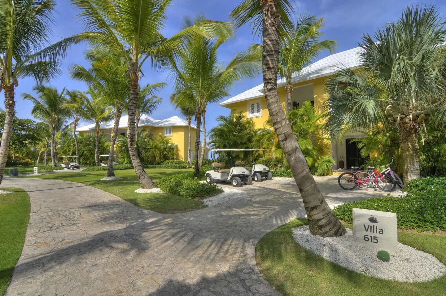 Palm-lined villa lane with golf carts, bicycles, and a Villa 615 sign at Tortuga Bay Hotel.