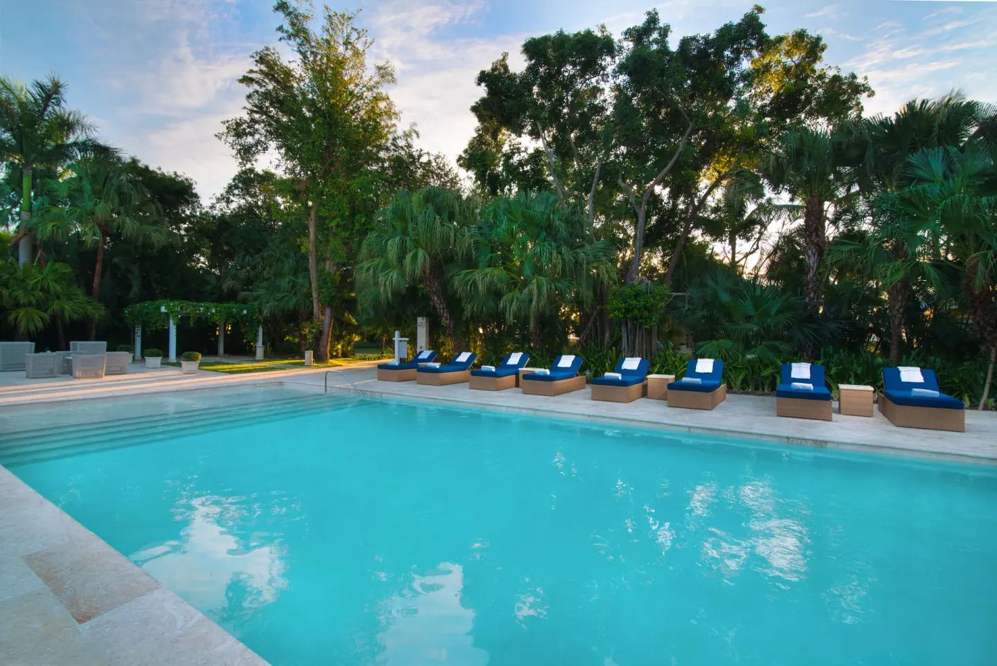 Pool lined with blue loungers and tropical trees at Tortuga Bay Hotel.