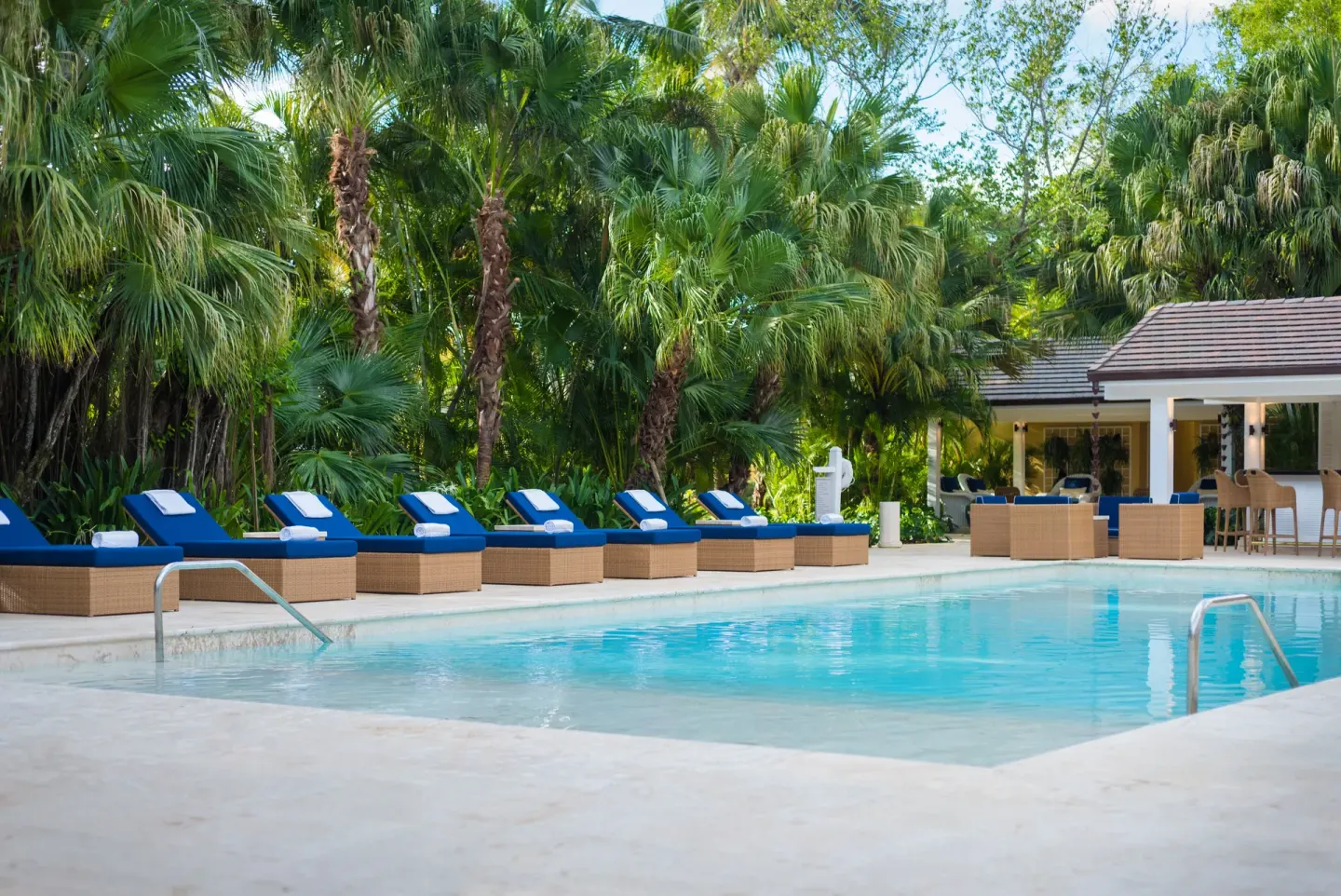 Pool deck with blue loungers, palms, and a shaded bar area at Tortuga Bay Hotel.