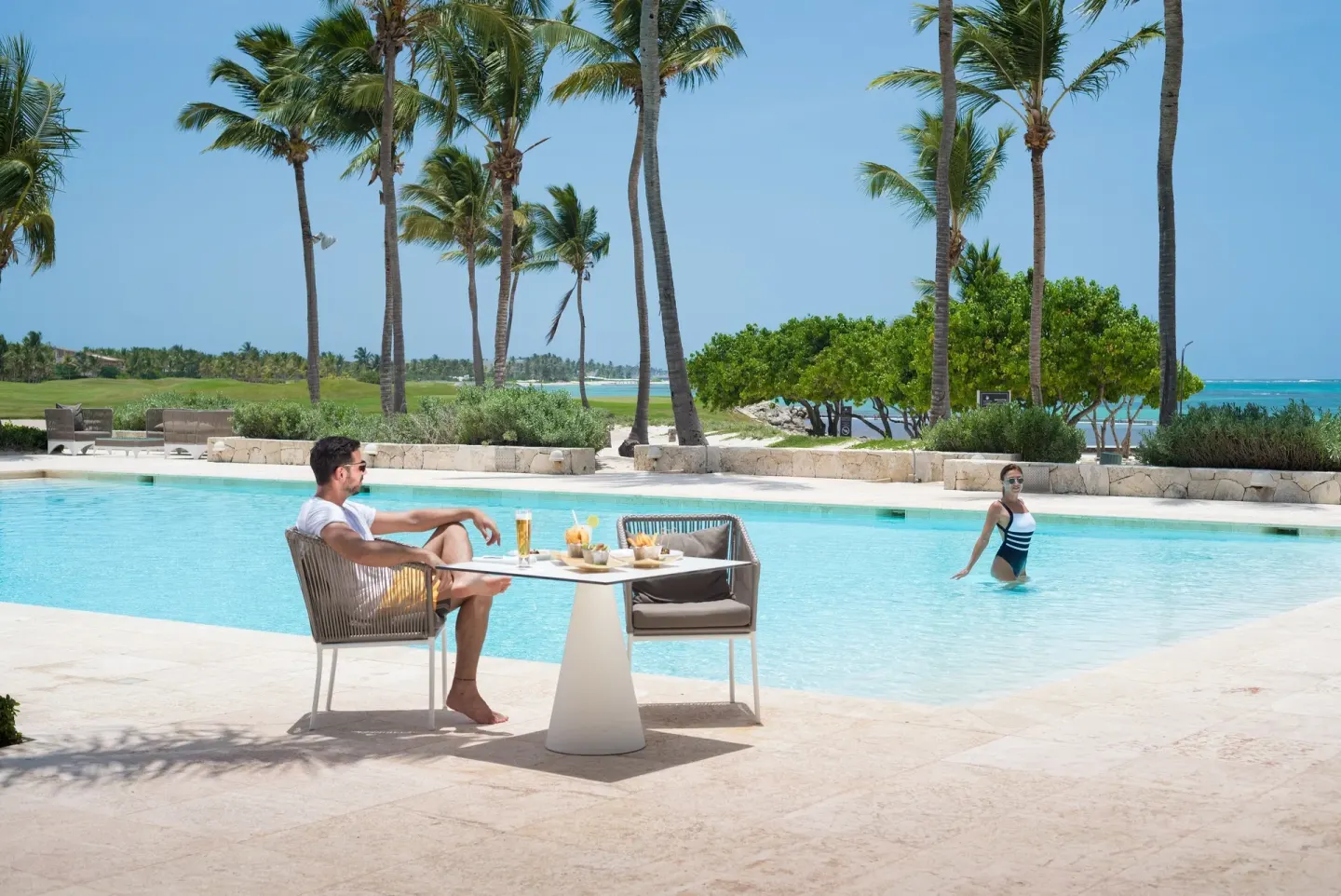 Guests relax by a palm-lined pool with the sea beyond at Tortuga Bay Hotel.
