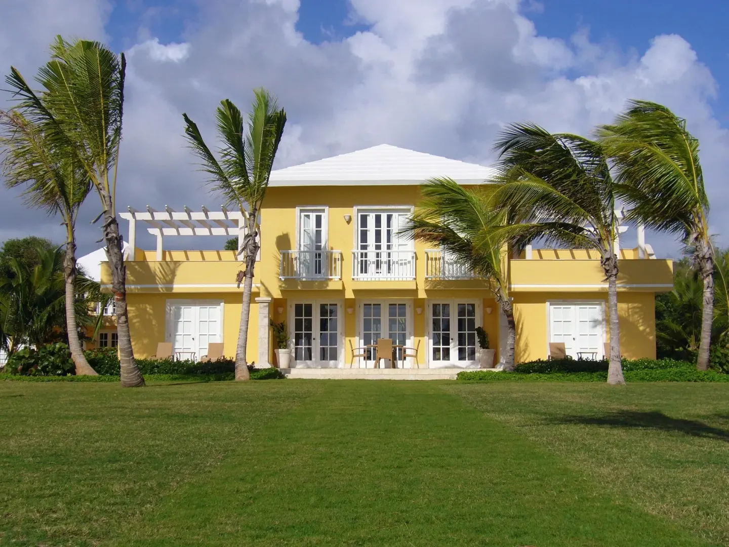 Yellow villa exterior with white balconies, palms, and lawn at Tortuga Bay Hotel.
