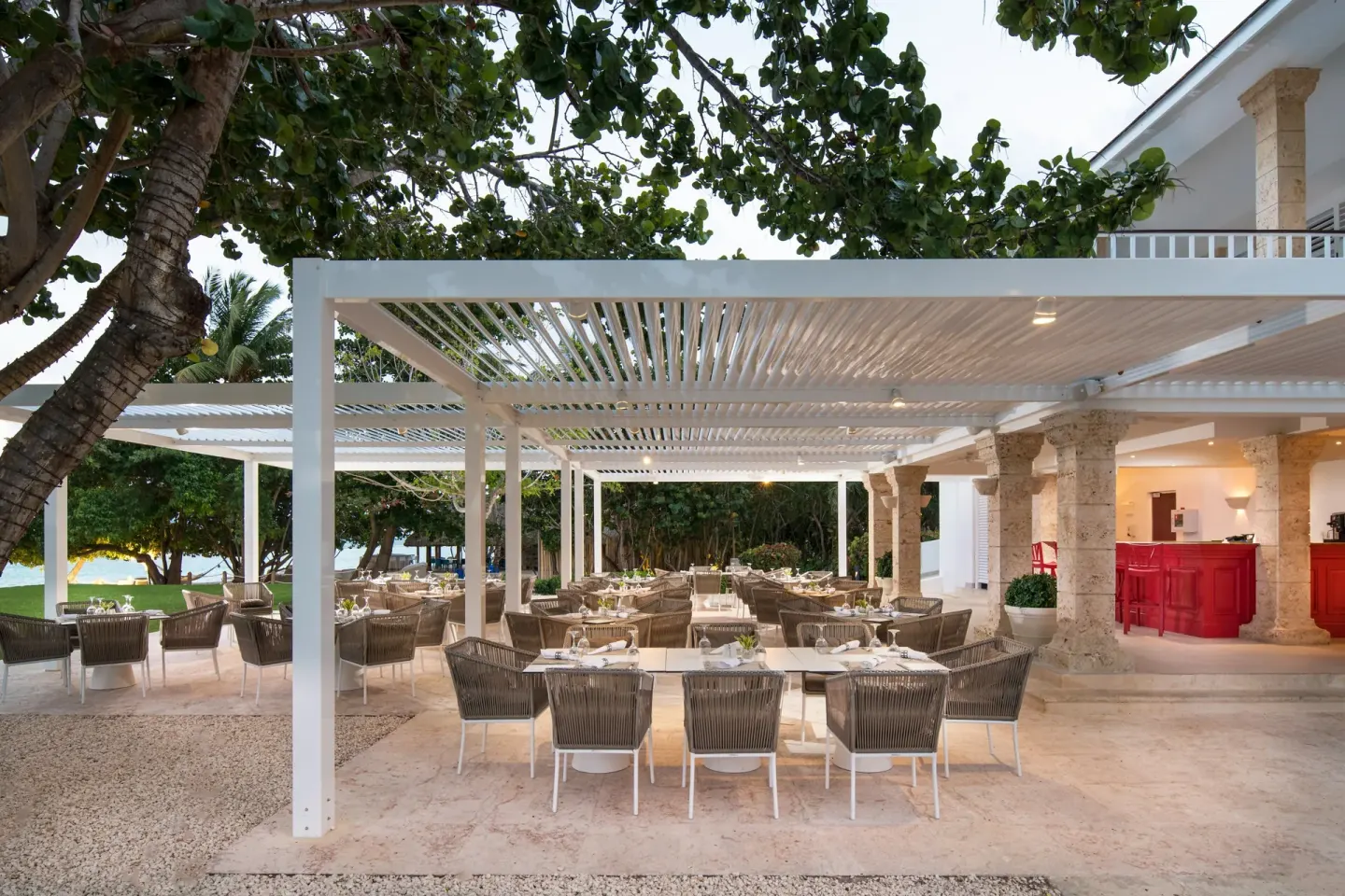 Outdoor dining tables sit under a white pergola near the beach at Tortuga Bay Hotel.