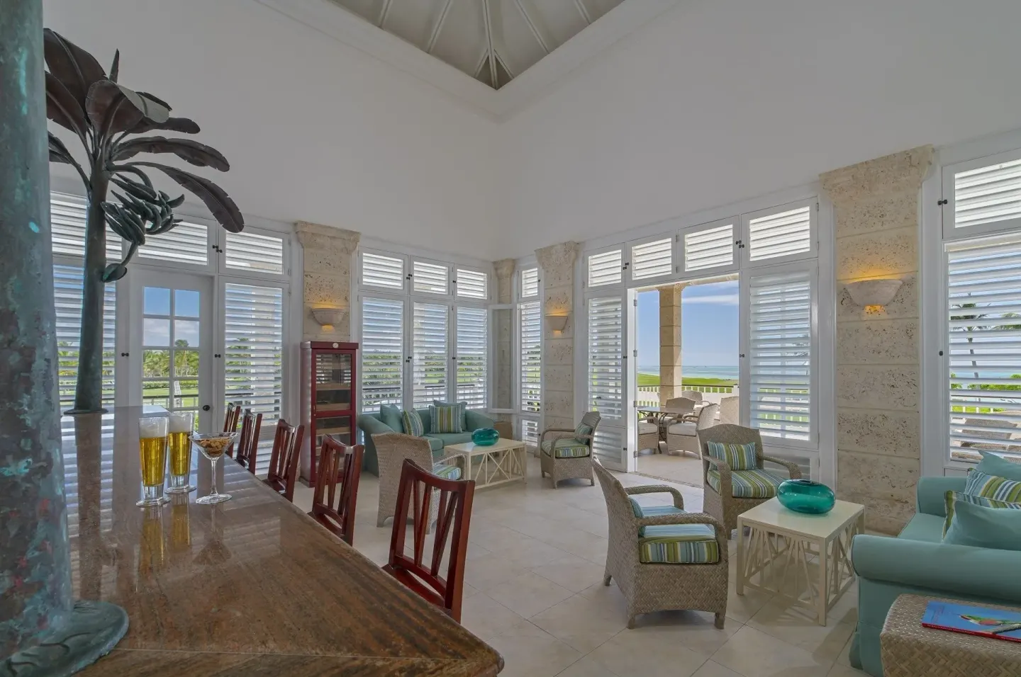 Bright lounge with shuttered windows, bar counter, seating, and ocean glimpses at Tortuga Bay Hotel.