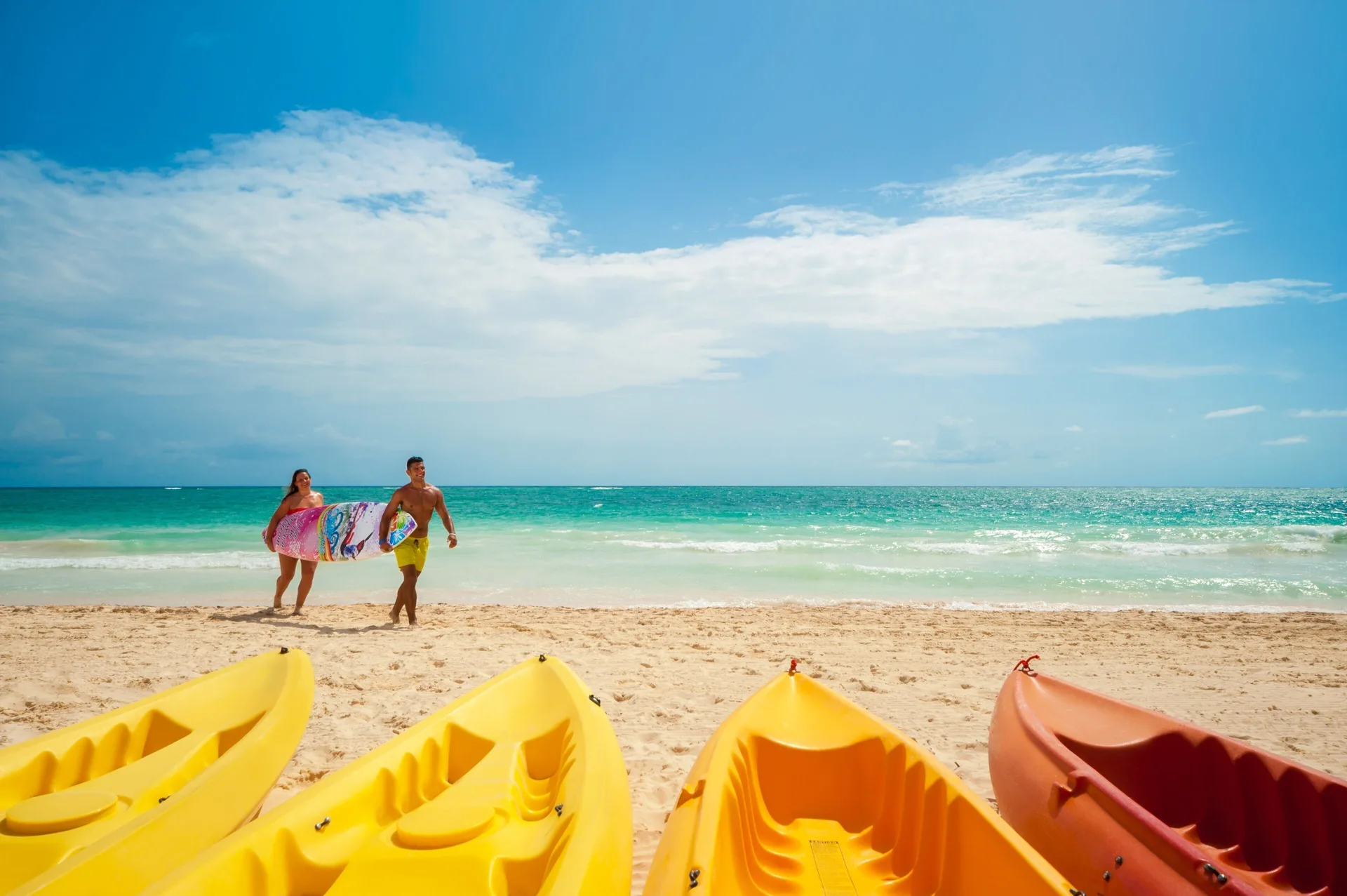 Kayaks line the beach as two guests walk by the ocean at Tropical Deluxe Princess.