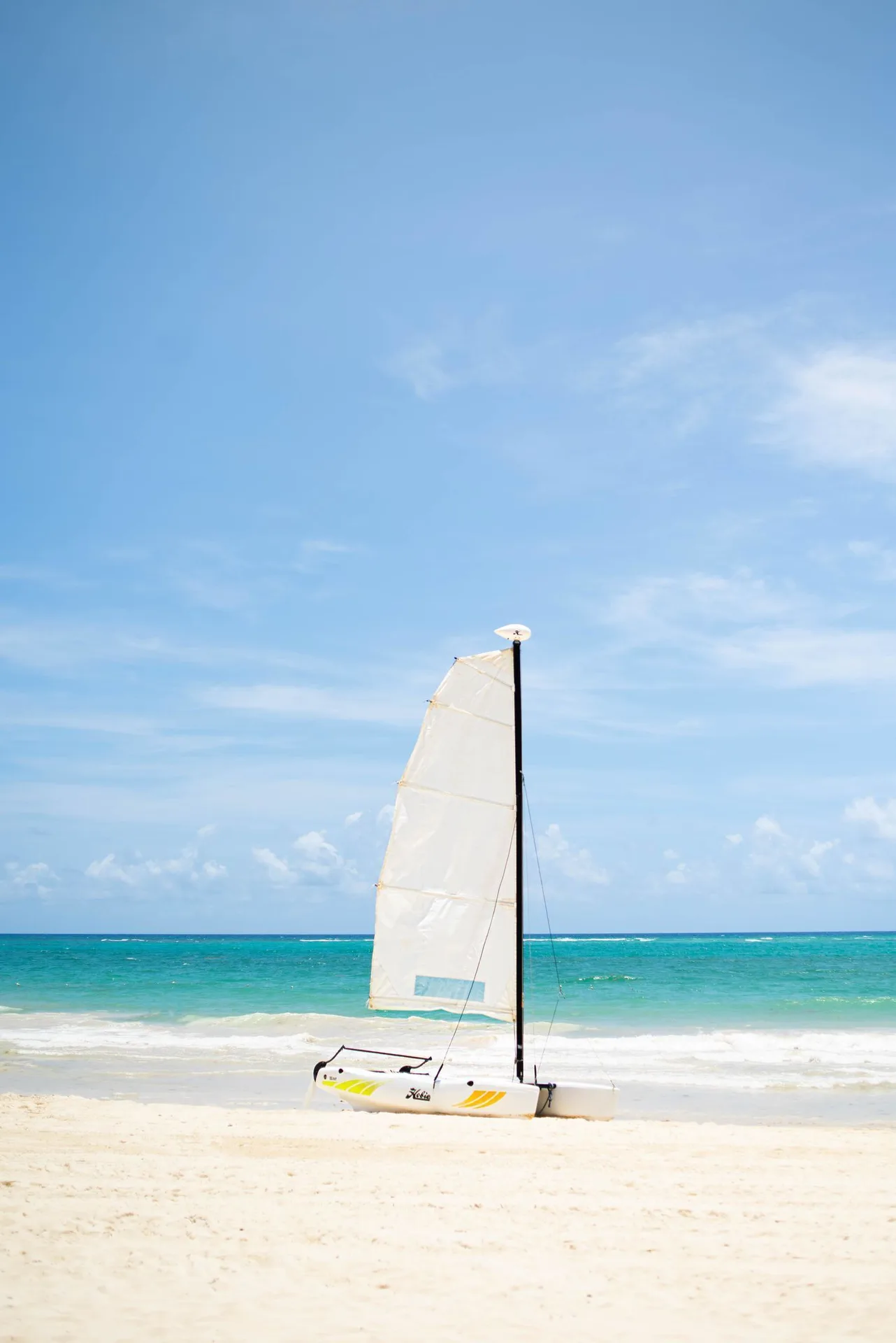 A small sailboat rests on the beach beside turquoise water at Tropical Deluxe Princess.