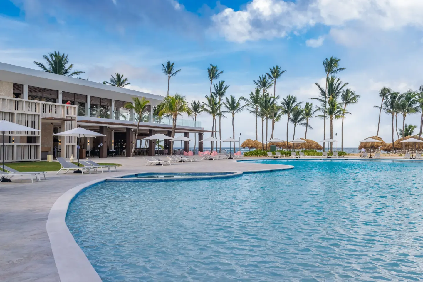 Beachfront pool with loungers, palms and a modern building at Tropical Deluxe Princess.